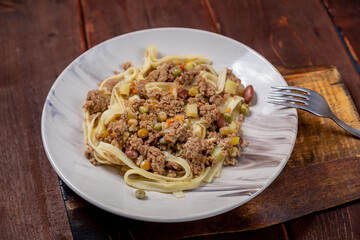 Noodles with minced meat and vegetables in sauce in a plate on the table