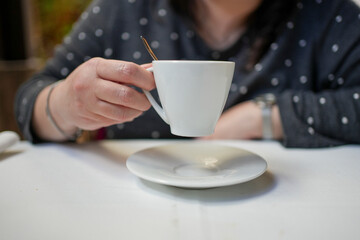 Woman holding white coffee cup and saucer in cafe