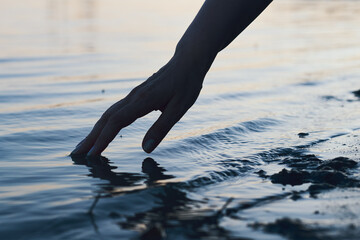 hand gently reaches towards the rippling water, creating a serene and reflective moment.