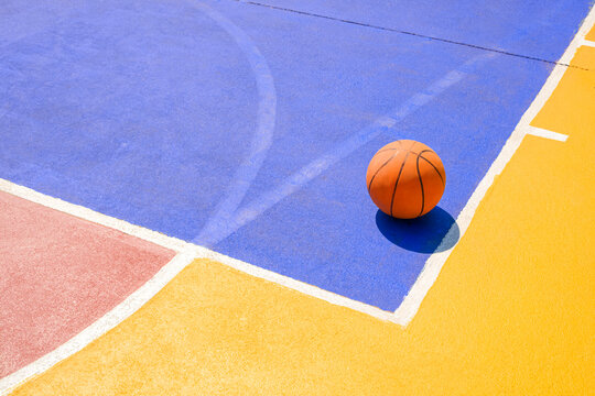 Basketball on outdoors basketball court with colorful pattern and white outline on concrete yard floor surface, sport field background