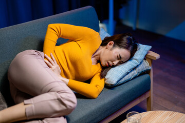 Woman experiencing stomach pain, reclining on living room couch and clutching abdomen