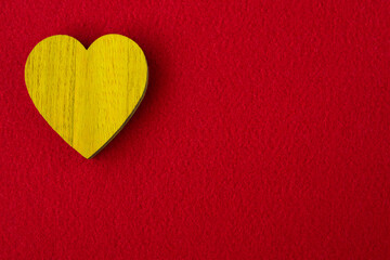 Obraz premium Yellow wood heart on the red fabric background with space for text.
