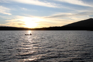 A landscape of a boat in the middle of a lake and a great sunset.