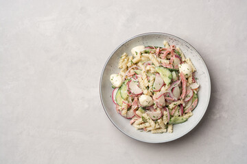 Pasta salad with vegetables, sausage and mozzarella cheese in plate on concrete background