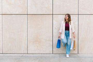 Happy shopper leaning against wall holding shopping bags