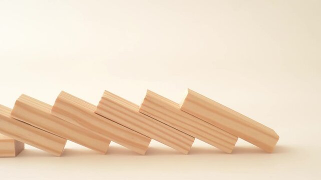 Wooden blocks falling in chain reaction on the pale orange background. Domino effect. Close-up.