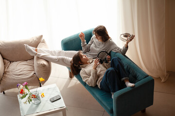 Two  teenagers girls  is relaxing at home in the living room in headphones, sitting in an armchair and sofa,  listening music in headphones