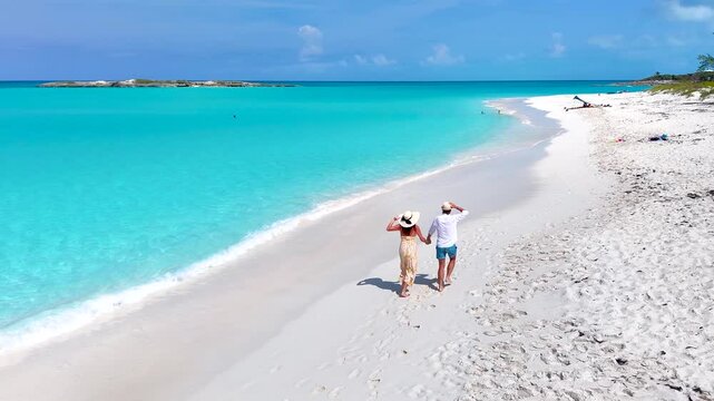 Aerial slow motion view of a happy vacation couple running on a tropical beach with turquoise ocean