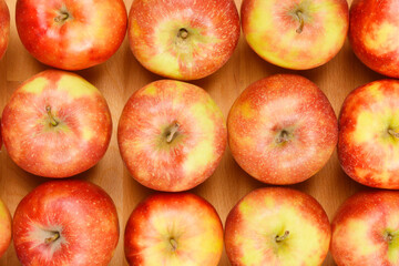 An overhead view of a grid of red and green apples, neatly arranged in rows on a wooden surface
