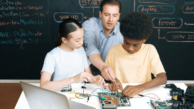 Smart mentor teach main board construction while diverse teenager learning system. Teacher explain about motherboard structure while academic student learning to use electronic equipment. Edification.