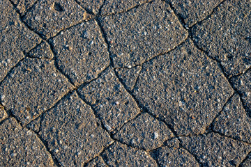 Cracks in asphalt, view from above. A close-up view of a fragment of old asphalt on a sunny day. A...