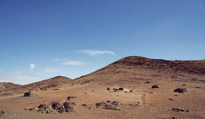 A barren desert landscape with rocky hills under a clear blue sky.