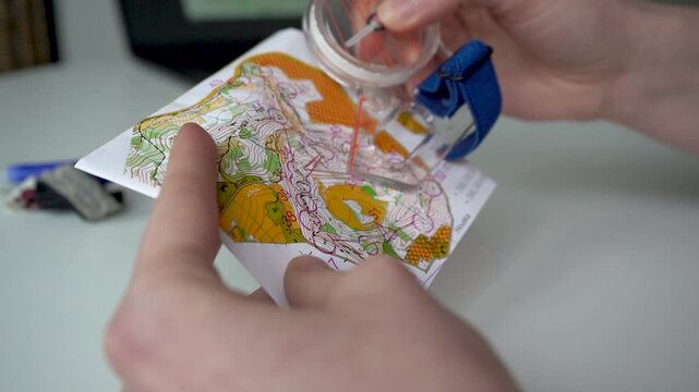 Holding a forest orienteering map in the hands and analyzing the course routes with a thumb compass