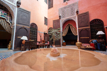 A traditional Moroccan courtyard with vibrant tiled flooring, a central fountain, and ornate...