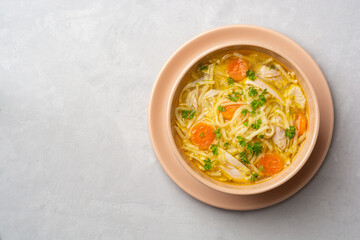 Chicken soup with noodles and vegetables in bowl on concrete background