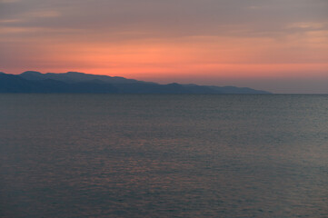 Serene sunset over tranquil waters with distant mountains creating a peaceful horizon view