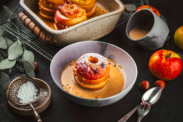 Traditional oven baked apples with crushed nuts, cinnamon and butter served with homemade vanilla sauce as close-up in a design plate