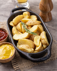 Rustic baked potatoes in a plate with ketchup, mustard and beer over wooden table
