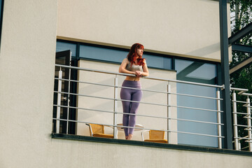 Fototapeta premium Beautiful girl stands on the balcony of a country cottage and enjoys a warm sunny morning