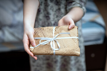pair of female hands gracefully presenting a rectangular gift wrapped in yellow mesh kraft paper,...