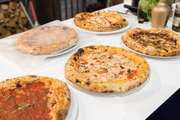 Multiple freshly baked pizzas with different toppings displayed on white table