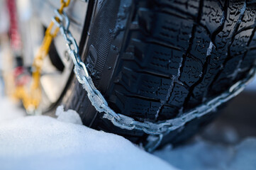 Close-up of a winter tire with snow chains covered in ice and snow, providing traction on slippery...