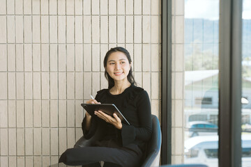 Dreaming of Innovation: An Asian businesswoman, deep in thought, engrossed in her tablet, poised in...