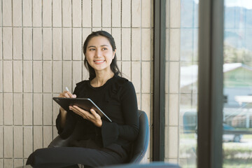 Serene Productivity: A focused woman sits indoors, holding a tablet, bathed in natural light,...