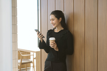 Modern Woman Relaxing: An Asian woman pauses during the day, leaning against a wooden wall near a...