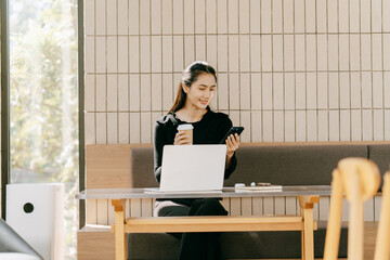 Laptop and Coffee Moment: A young, professional woman, focused on her phone, sipping a beverage...