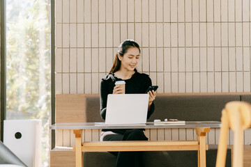 Modern Workspace: A young woman engrossed in her work, sipping coffee and navigating her smartphone...