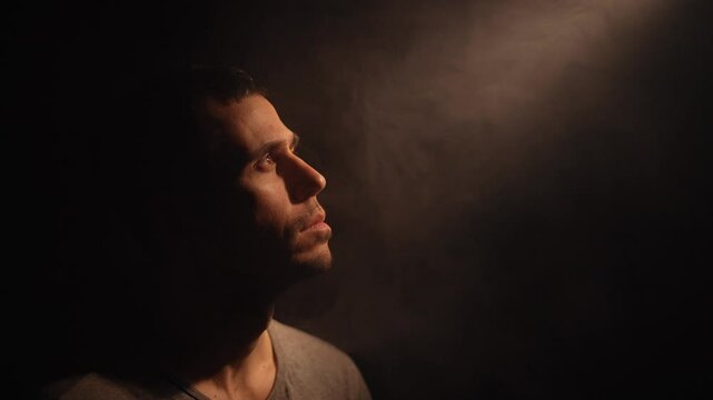 Man gazes upward as divine light pierces surrounding darkness