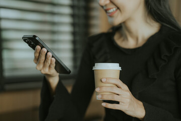 Coffee and Connectivity: An attractive person engrossed in their smartphone while holding a cup of...