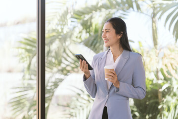 Modern Professional Serenity: A sophisticated businesswoman pauses by a sunlit window, phone in...