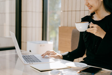 Morning coffee and productivity: A young woman sits at a desk with a laptop and cup of coffee,...