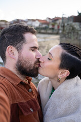 Fototapeta premium Romantic couple kissing on cobblestone street, traditional horreos framing picturesque coastal scene in combarro, galicia, spain