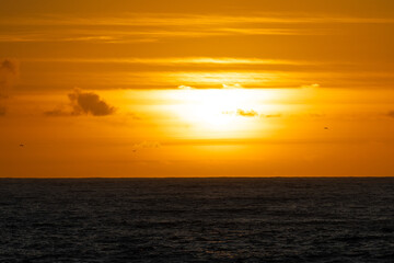 Fototapeta premium Golden sunlight illuminating dramatic sky, painting clouds in warm tones while casting soft glow over serene ocean waters near punta faxilda coastline
