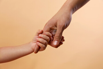 Father and child holding hands on beige background, closeup