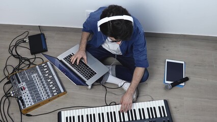 Young man in sound recording studio. Guy sit on floor and work with laptop and soung mixing...