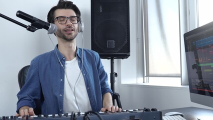 Young man in sound recording studio. Cheerful positive guy playing on keyboard and singing....