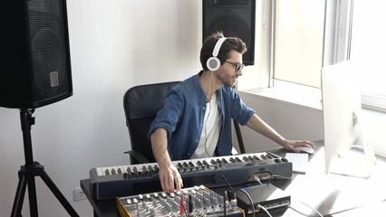 Young man in sound recording studio. Guy sit in front keyboard and using music mixing console....