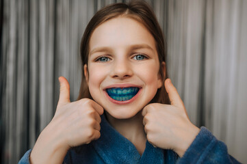 Close-up photo, portrait of beautiful happy smiling child girl face with blue silicone denture,...