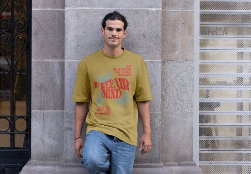 Man in short sleeve t-shirt poses against a stone wall in Barcelona during daylight. Mockup ready to use