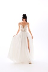 Fototapeta premium Elegant model poses in a flowing white dress with intricate details and a high slit in a bright studio setting during a fashion shoot