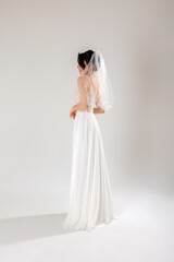 Fototapeta premium Elegant bride in white gown with veil poses gracefully in a studio setting before her wedding day