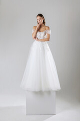 Fototapeta premium Elegant bride in a delicate white gown poses gracefully on a pedestal in a minimalist studio setting