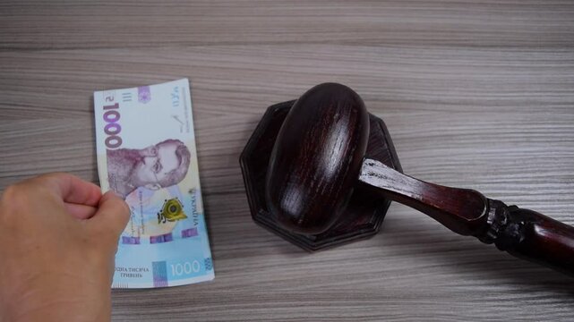 Near the ceremonial wooden gavel of the judge, the hand places a stack of one-thousandth Ukrainian hryvnia banknotes. C oncept of corruption, bribes and venality of the judicial system.