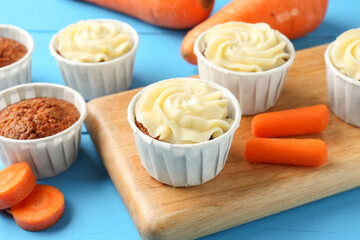 Tasty carrot muffins with fresh vegetables on light blue wooden table, closeup
