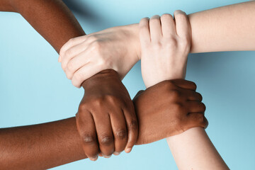 Stop racism. People of different skin colors joining hands on light blue background, closeup