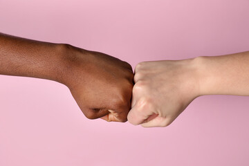 Stop racism. People of different skin colors bumping fists on light pink background, closeup